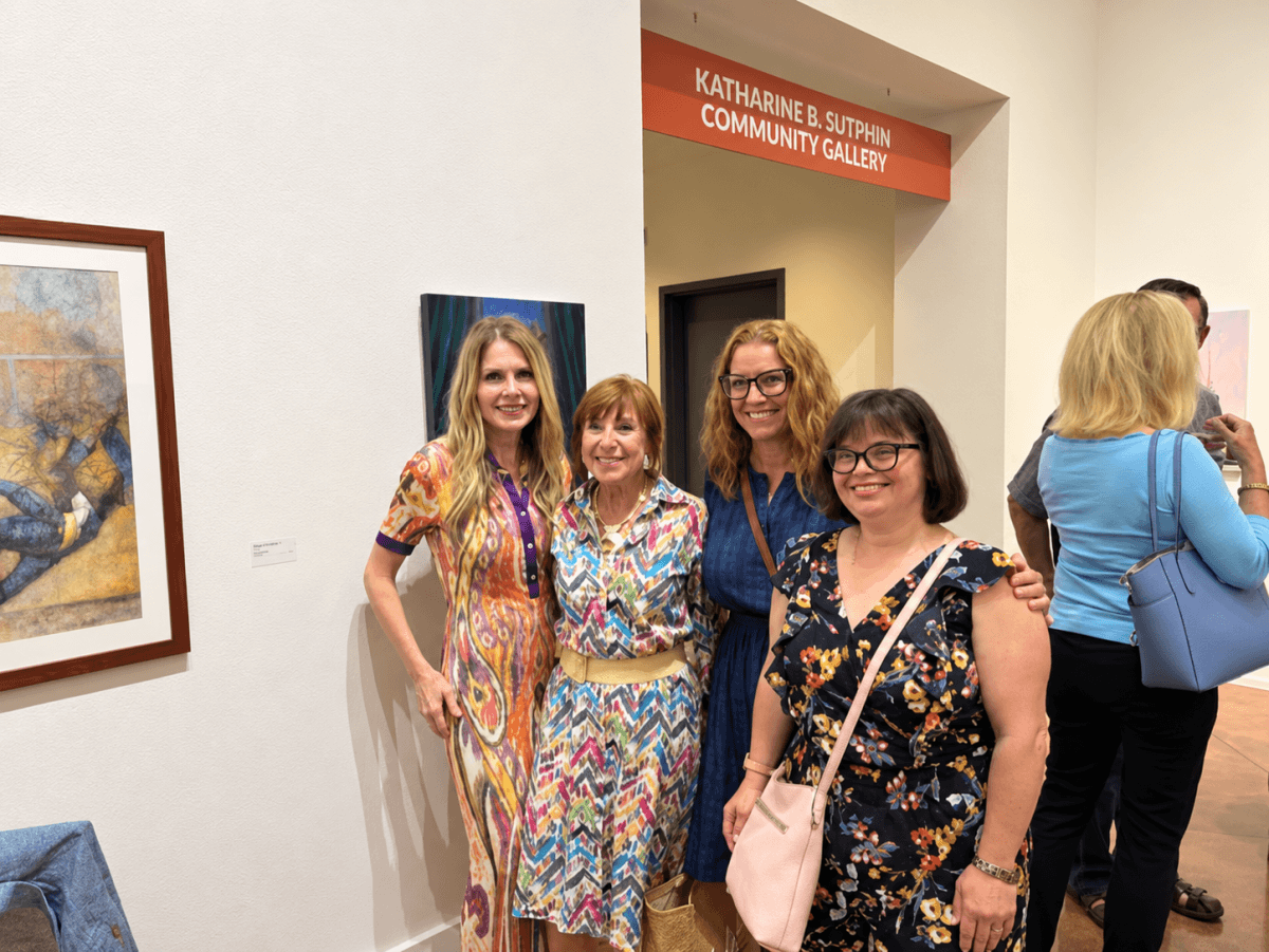 Four women pose together in front of framed artwork in a gallery labeled “Katharine B. Sutphin Community Gallery.”.