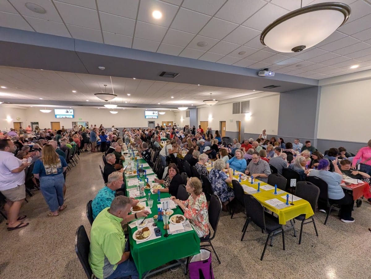 A packed banquet hall of Bingo Night guests seated at long tables with green and yellow tablecloths
